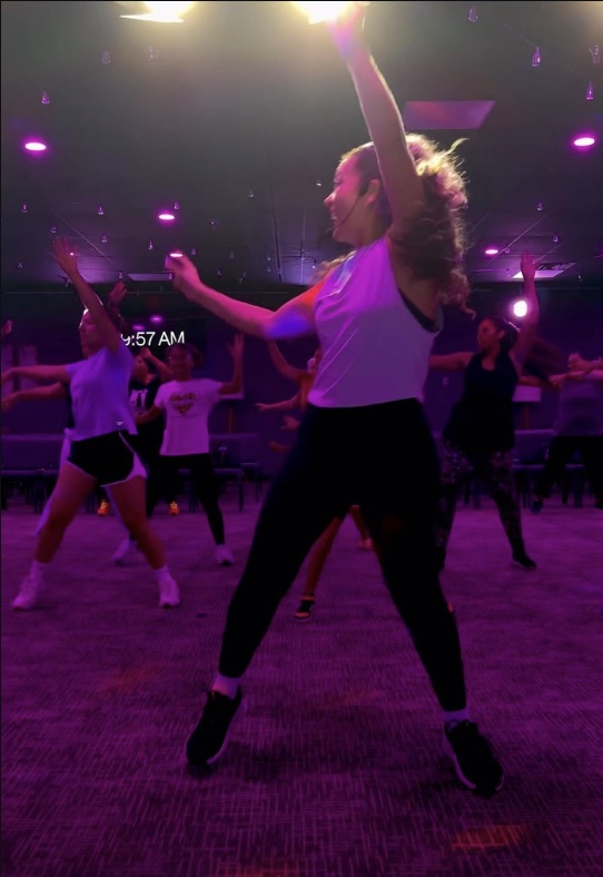 An Enough7Fitness cardio dance class mid-song, arms up under the lights